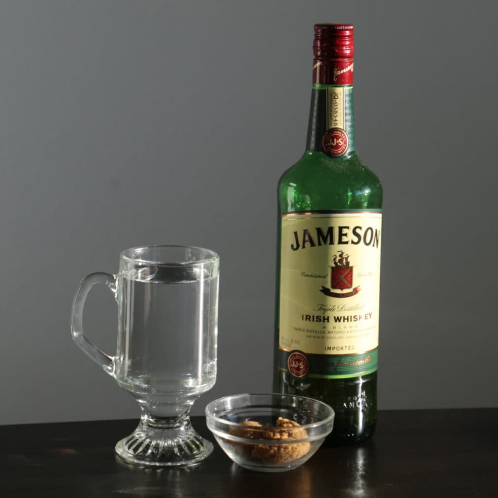 Bottle of Jameson Irish Whiskey and a cup of hot water letting the glasss warm before making the drink