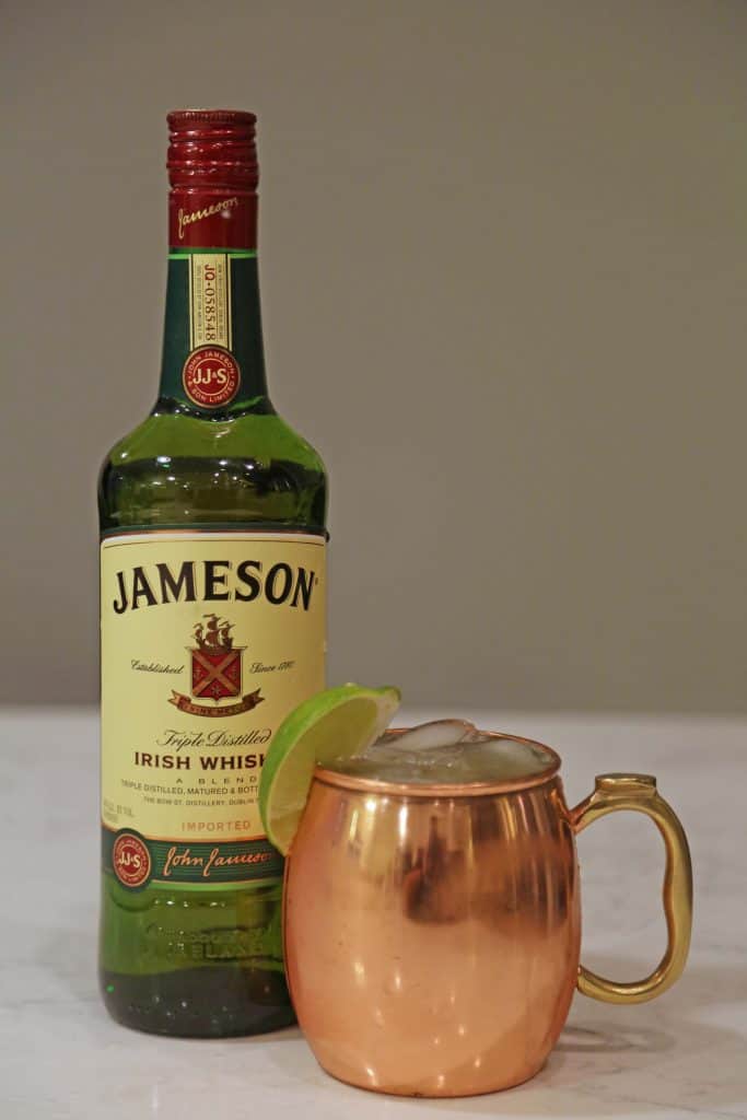 Bottle of Jameson Irish Whiskey next to a copper mug with a lime and cocktail
