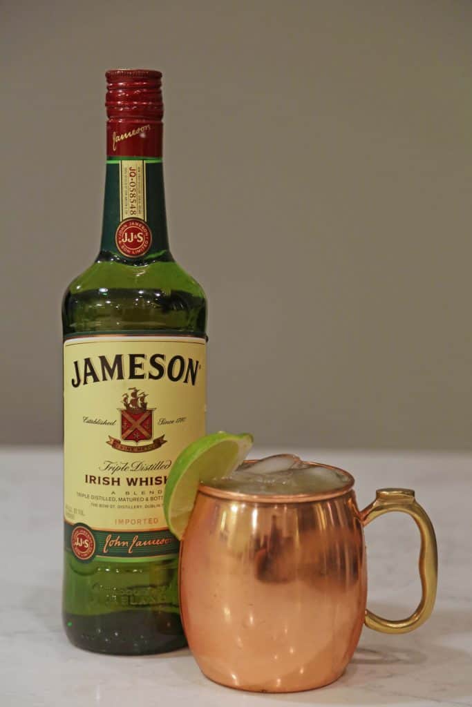 Bottle of Jameson Irish Whiskey next to a copper mug with a lime and cocktail 