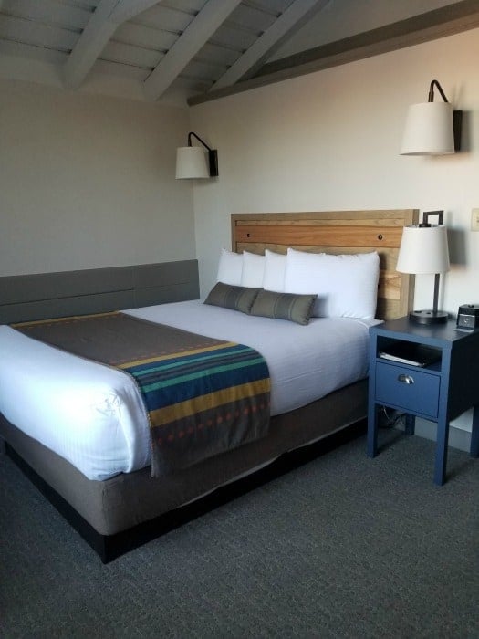 Queen bed with 2 lamps over it and a bed side table inside Bright Angel Lodge Cabin