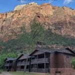 Photo of the Zion Lodge with red cliff in the background with text "Zion Lodge Zion National PArk by ParkRangerJohn.com"