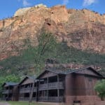 Photo of The Zion National Lodge with red cliff in the background and text reading "Zion National Park Lodge by ParkRangerJohn.com"