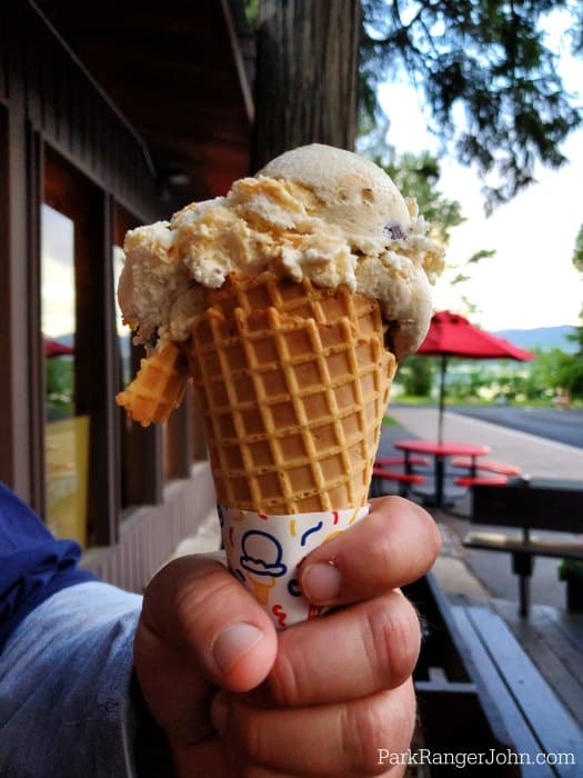 Hand holding a waffle cone with ice cream, red umbrella and Lake McDonald in the background. 