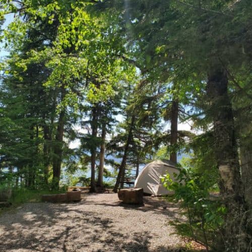 photo of a campsite with a tent and lake mcdonald in the background with text" Sprague Creek Campground Glacier National Park by ParkRangerJohn.com"