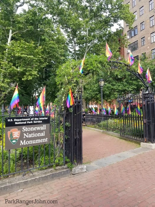 Entrance to Christopher Park in New York with a sign for Stonewall National Monument and Rainbow Flags