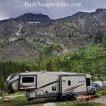 Photo of a 4th wheel trailer in a campsite at Two Medicine Campground with text "Two Medicine Campground Glacier National Park by ParkRangerJohn.com"