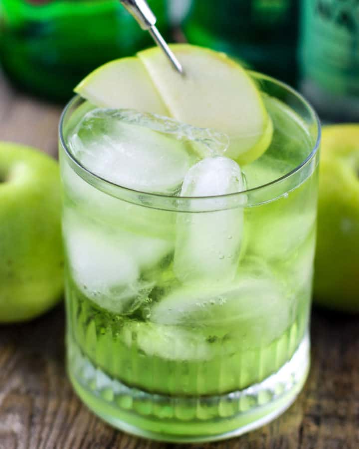 Green Irish Sour Apple Cocktail on a wood board with apples