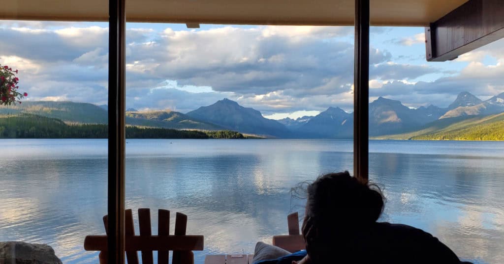 Sitting in an Adirondack chair relaxing on the porch staring over Lake McDonald and the Mountains from the porch at THe Village Inn at Apgar Hotel in Glacier National Park