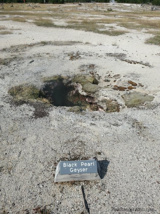 Dark hole surrounded by brown/grey rocks and steam in the background