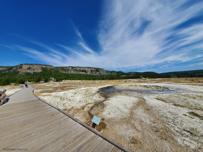 Biscuit basin wooden boardwalk along the left side next to Jewel Geyser with white clouds above