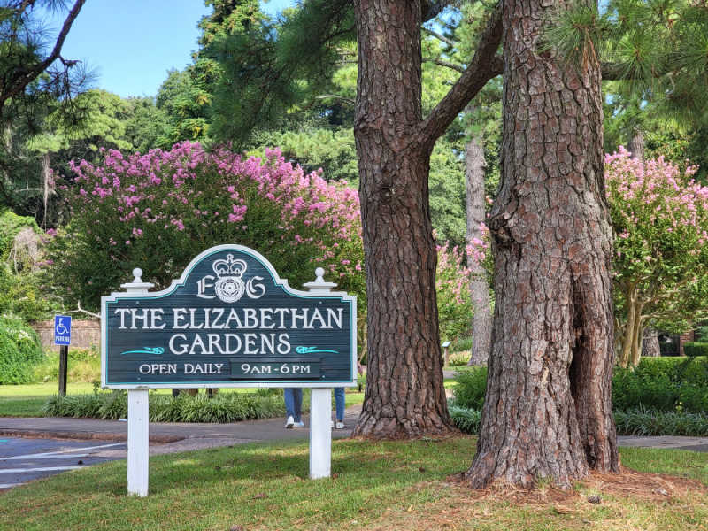 The Elizabethan Gardens sign near trees and flowering bushes