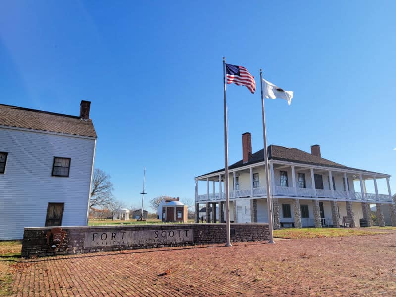 Entrance Sign for Fort Scott NHS with flag poles and historic buildings