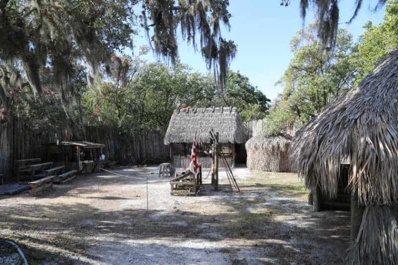 Camp Ucita in De Soto National Memorial with thatched roof buildings, a flag, and weapons