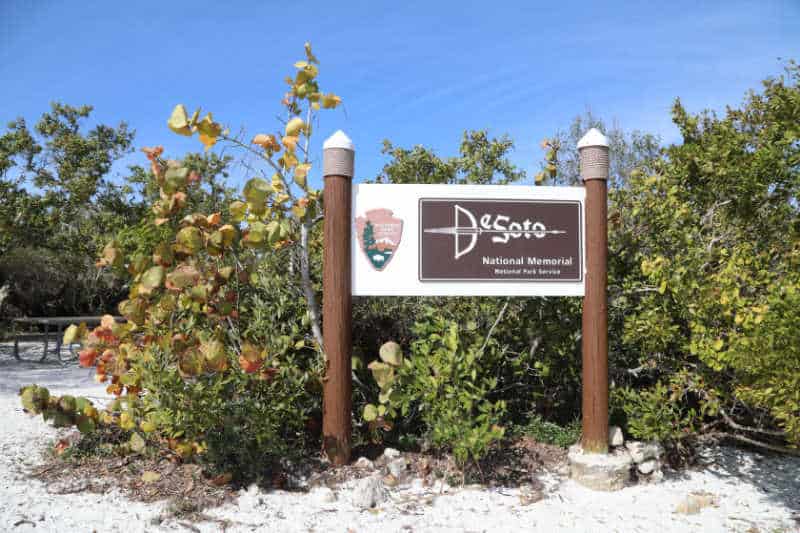 De Soto National Memorial Entrance Sign surrounded by green bushes and sand