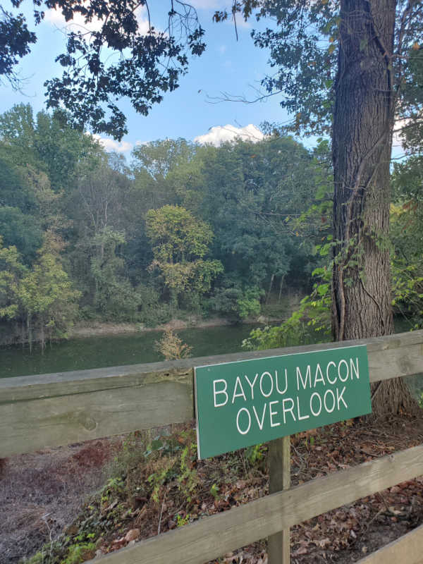 Bayou Macon Overlook sign on a fence overlooking water and trees in Poverty Point NM