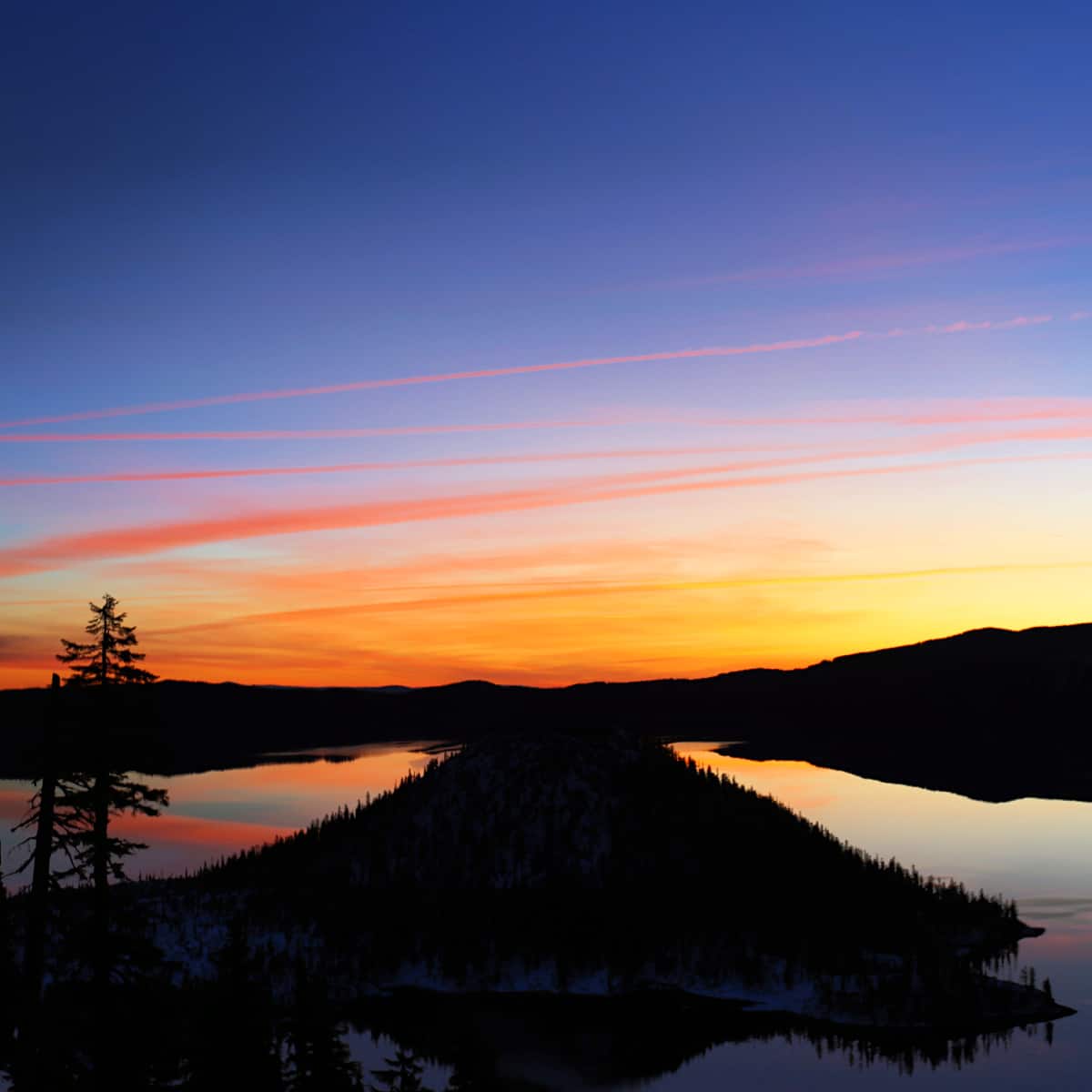 Colorful sunrise over Crater Lake National Park with a tree and island showing