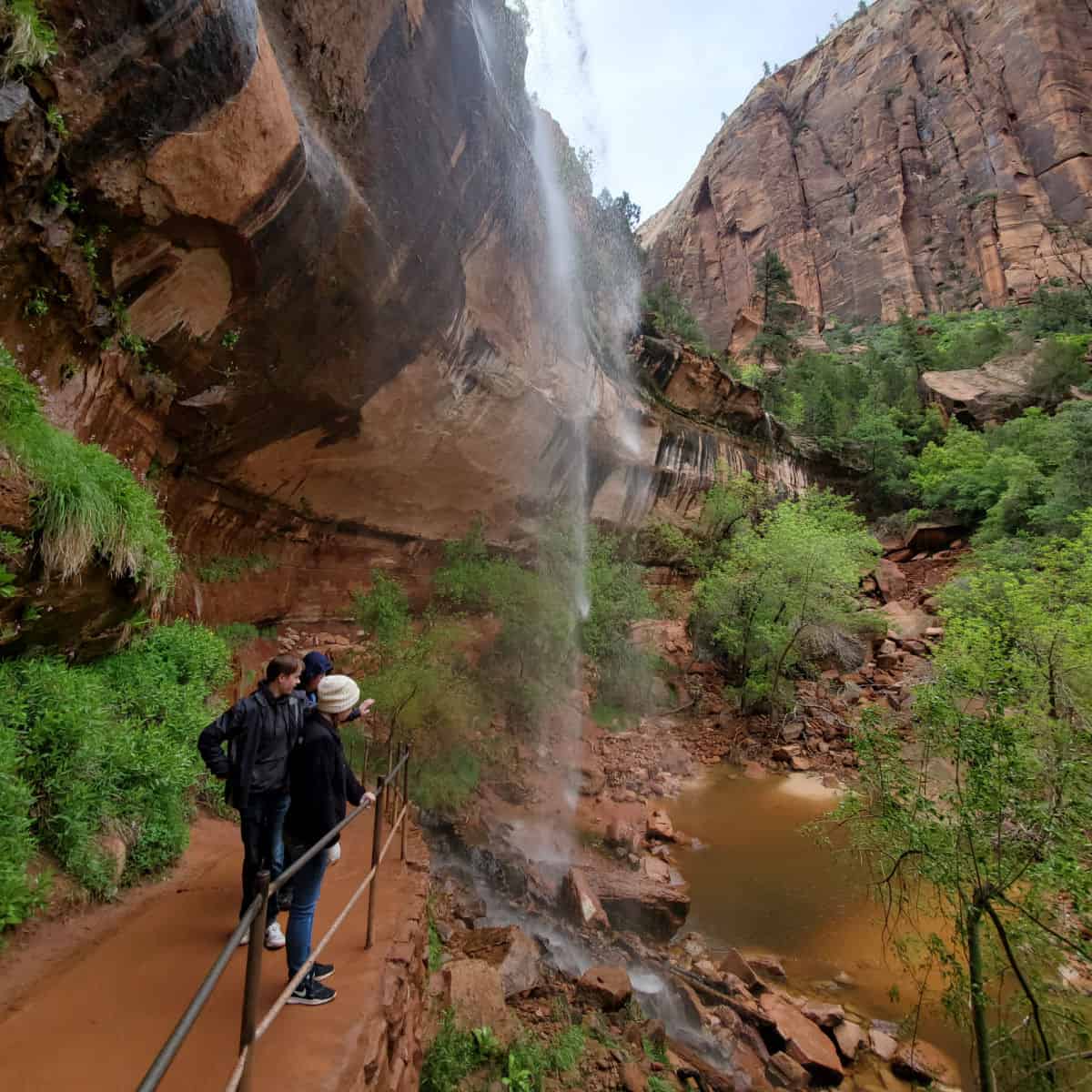 People pointing from trail with guard rail to a waterfall in red rocks