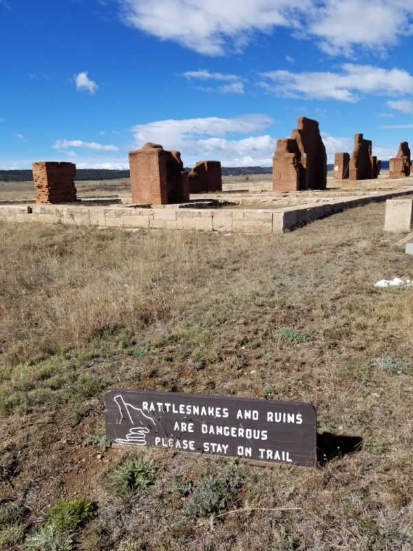 Rattlesnake warning sign in front of historic ruins in Fort Union National Monument