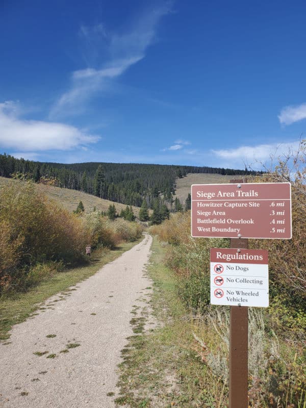 Siege Area Trails sign with a dirt hiking trail leading towards a mountain in Big Hole National Battlefield