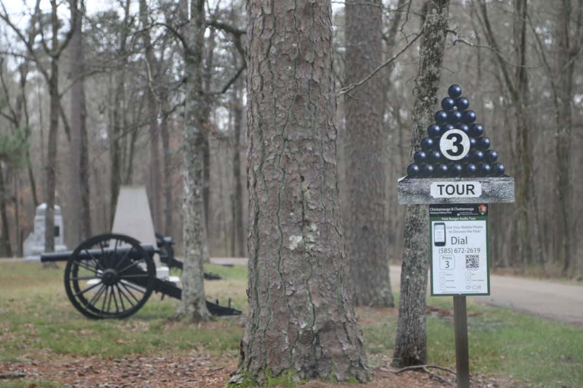 historic cannon behind a cell phone tour sign and trees