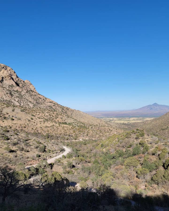 Dirt road leading through a large mountain valley with blue skies