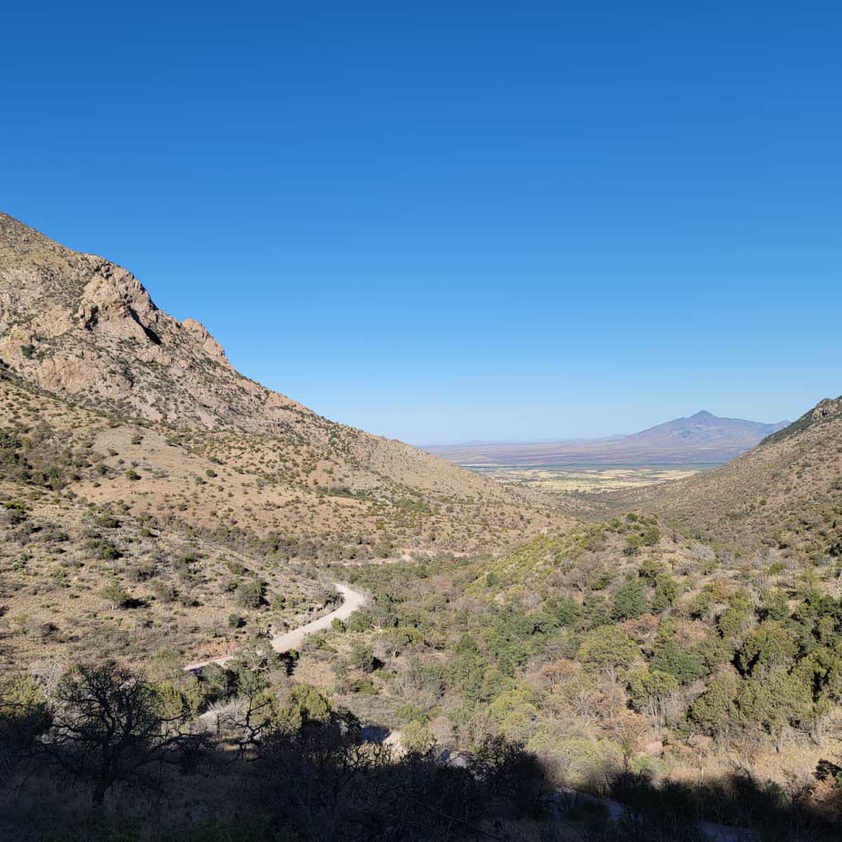 Dirt road leading through a large mountain valley with blue skies