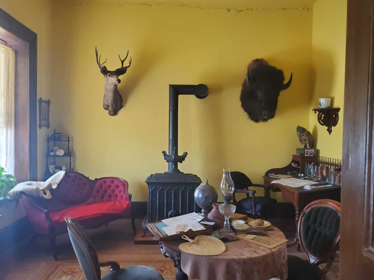 Historic Fort Larned living room with deer and bison head on the wall, owl, fireplace, table, and red couch
