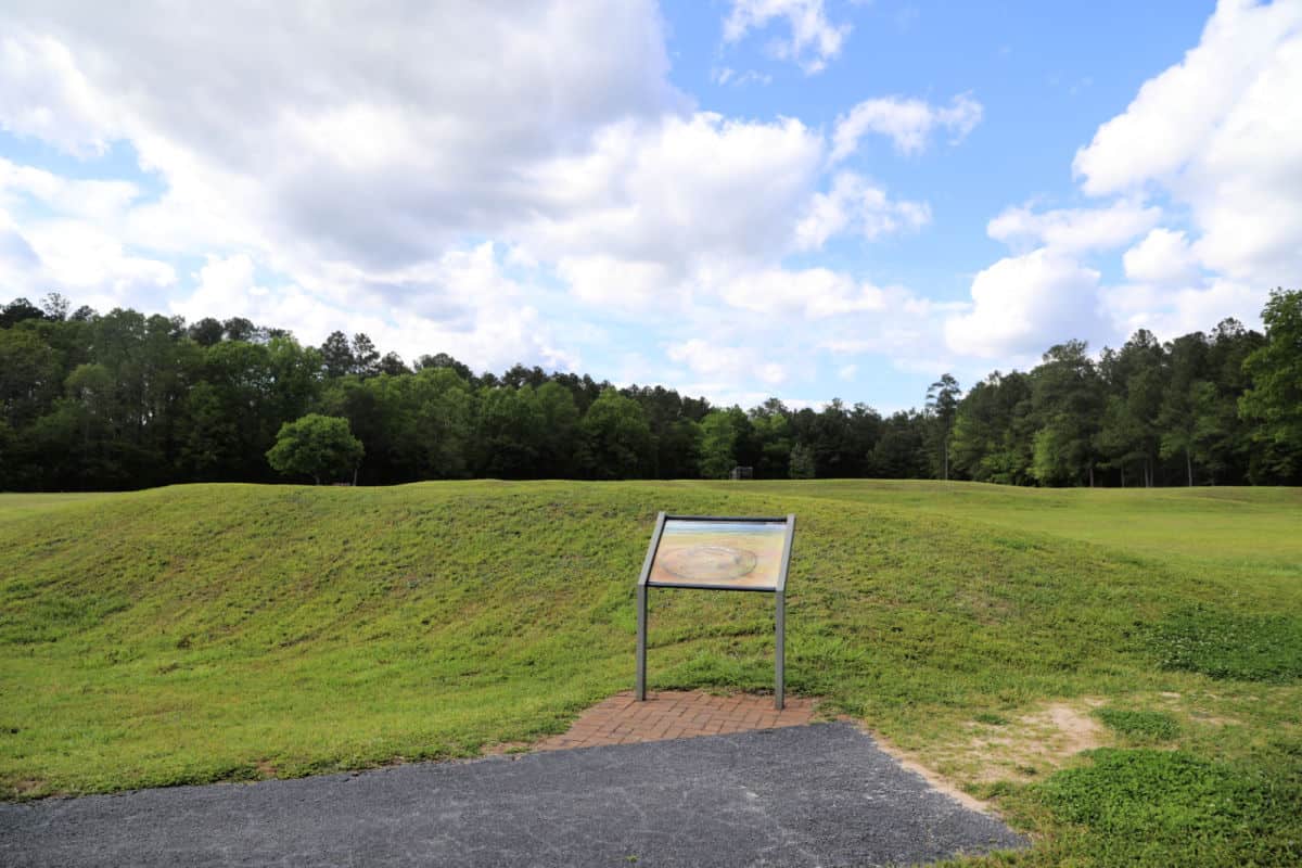 Interpretive panel in front of green mounds from star fort