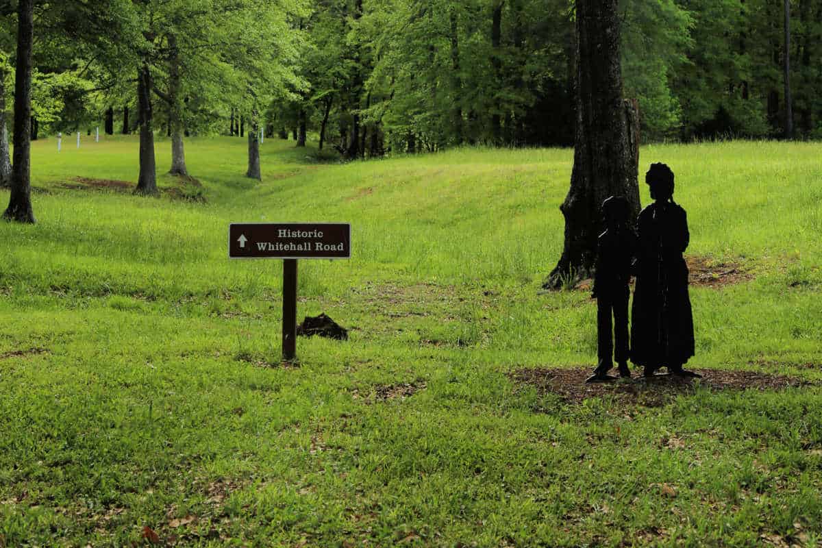 Historic Whitehall Road sign next to a black sculpture cut out of a woman and a child along a historic trail