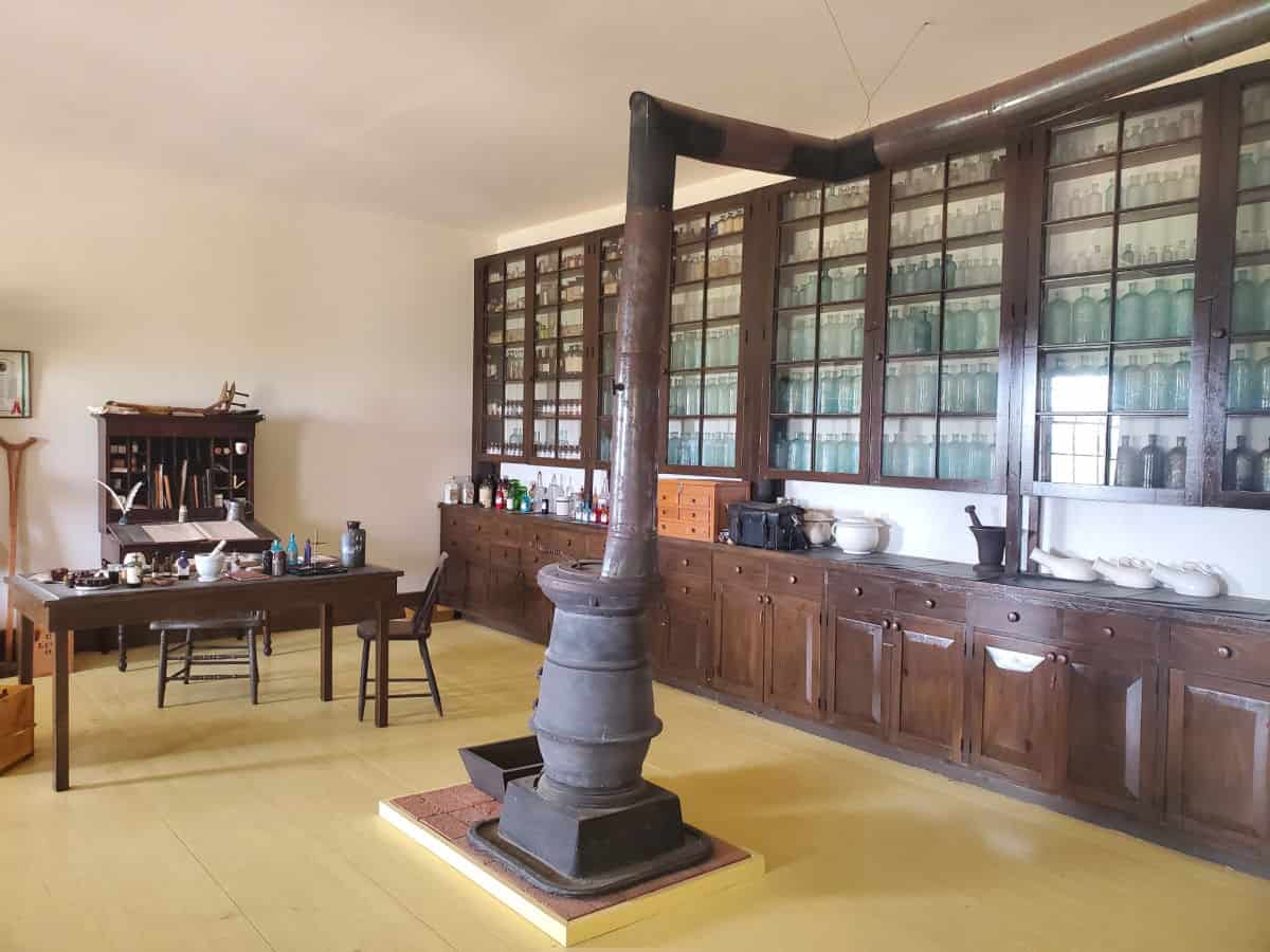 Pharmacy in Fort Larned with a fire place, and wall of glass bottles with a desk nearby