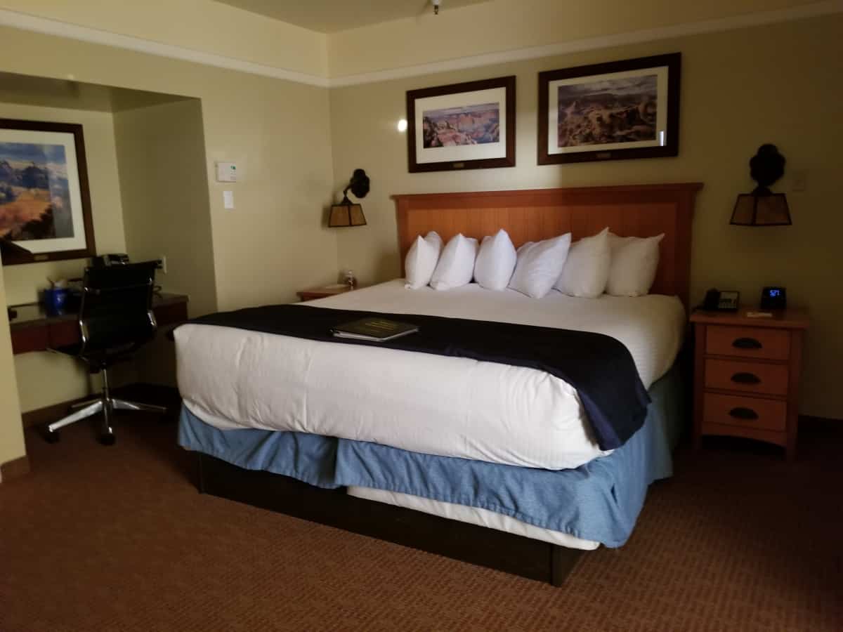 King bed with photos of the Grand Canyon over it, a nightstand, and a desk with a chair at the El Tovar Lodge