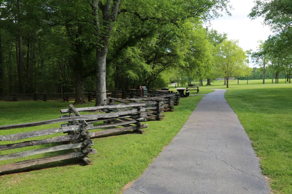 Paved walking trail next to wooden fence and green grass fields