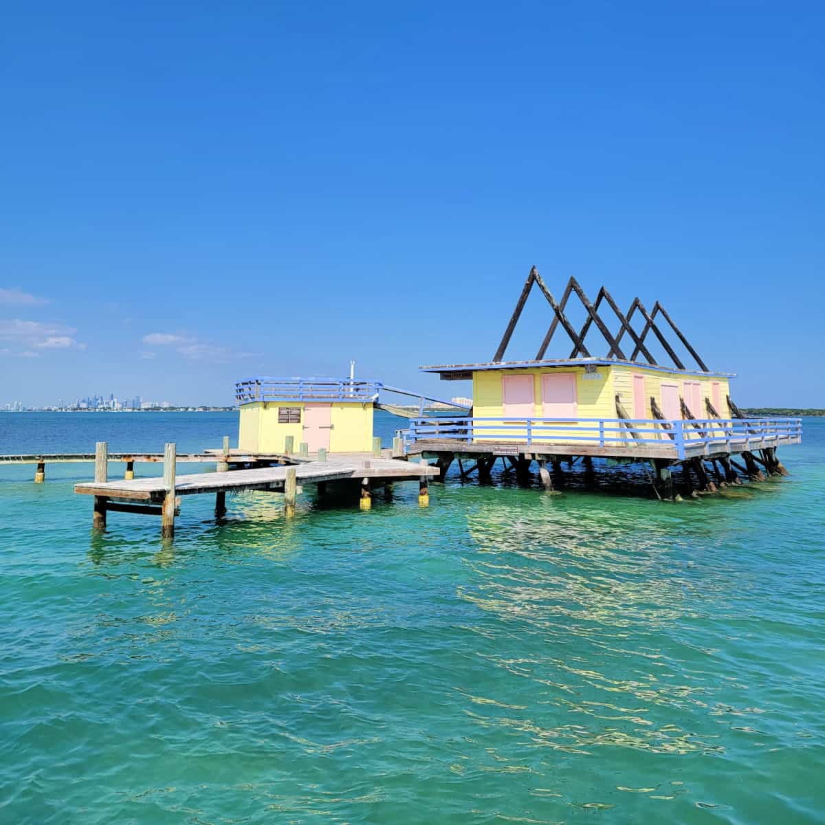 Stilltsville pink and yellow house with dock with the city of Miami in the background on Biscayne Bay