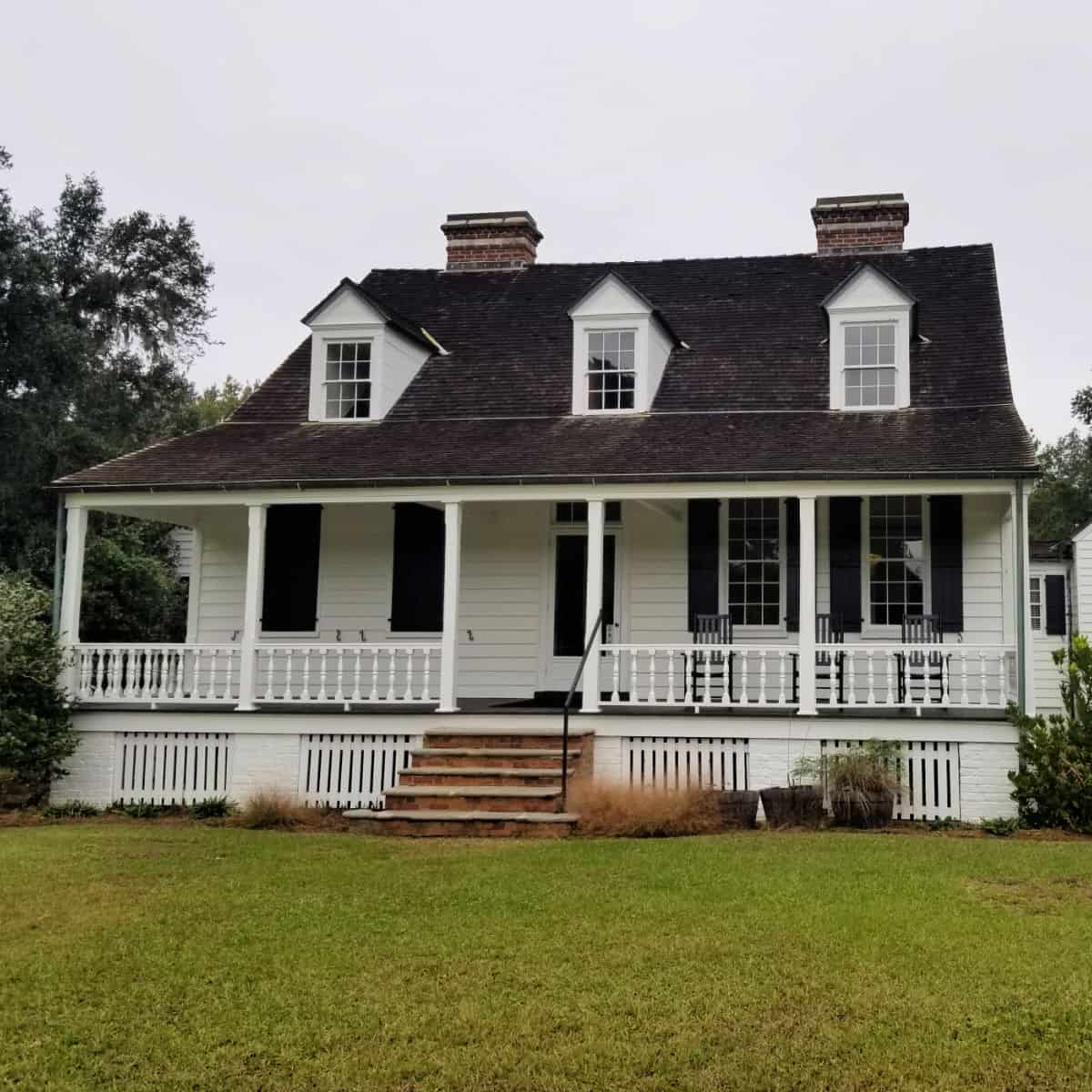 historic white house with steps leading up to a front porch with rocking chairs