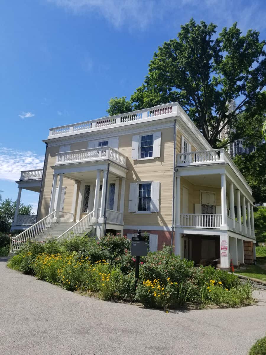 Historic Hamilton Grange with stairs leading into the house, balconies, and flowers planted around it