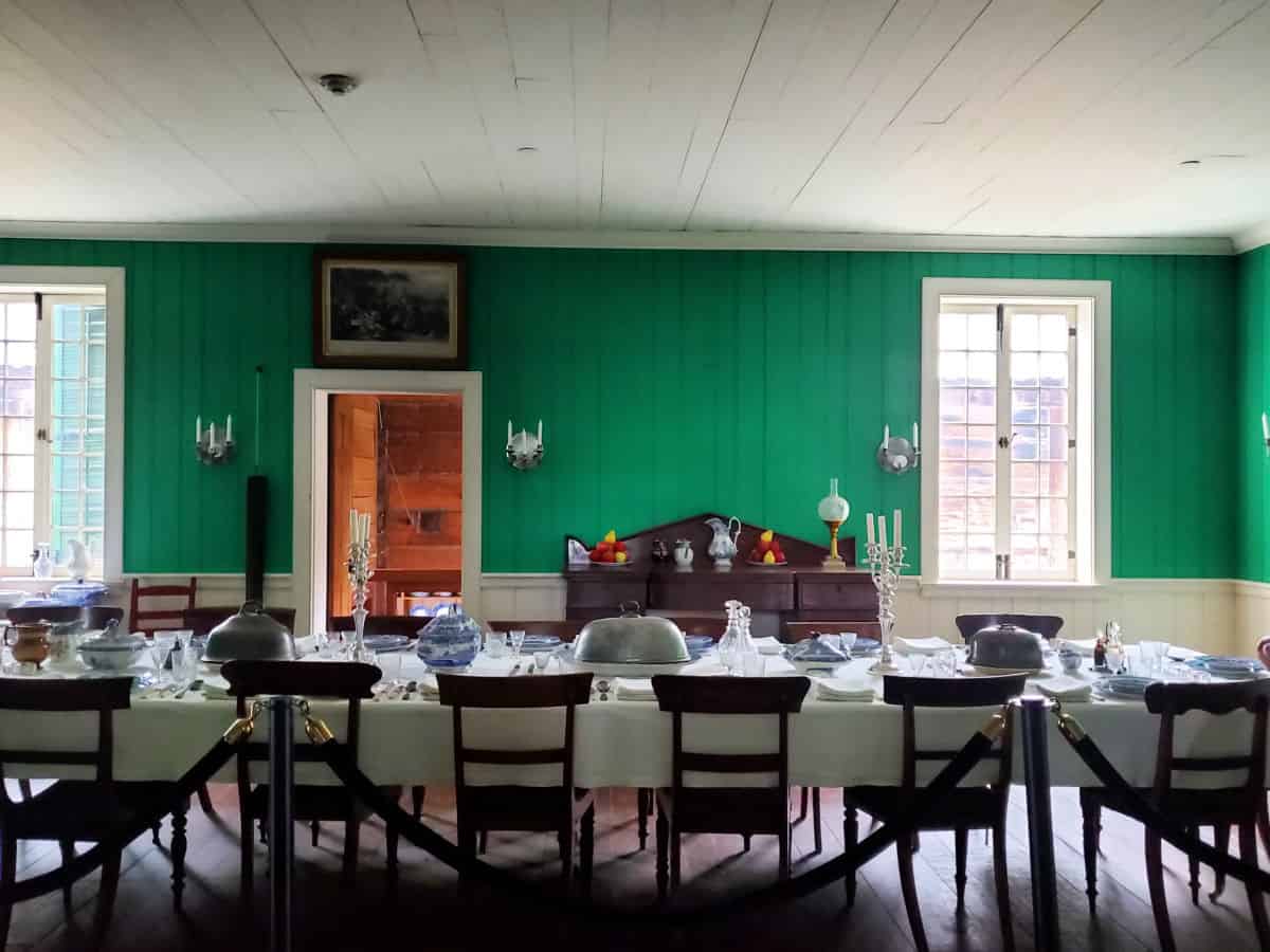 historic dining room with green walls, a long table with chairs, and table settings. 