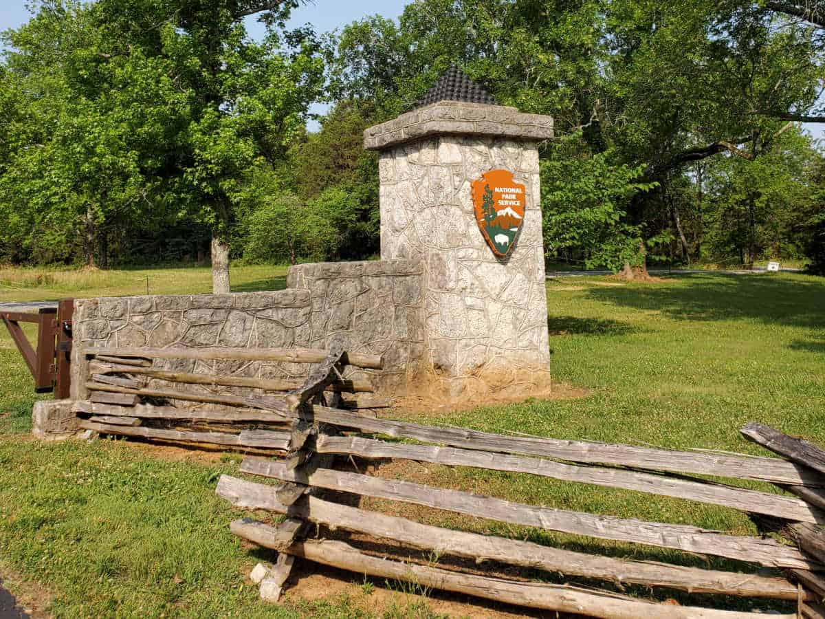 Wooden fence next to a stone pilar with the national park service emblem and a stack of cannon balls