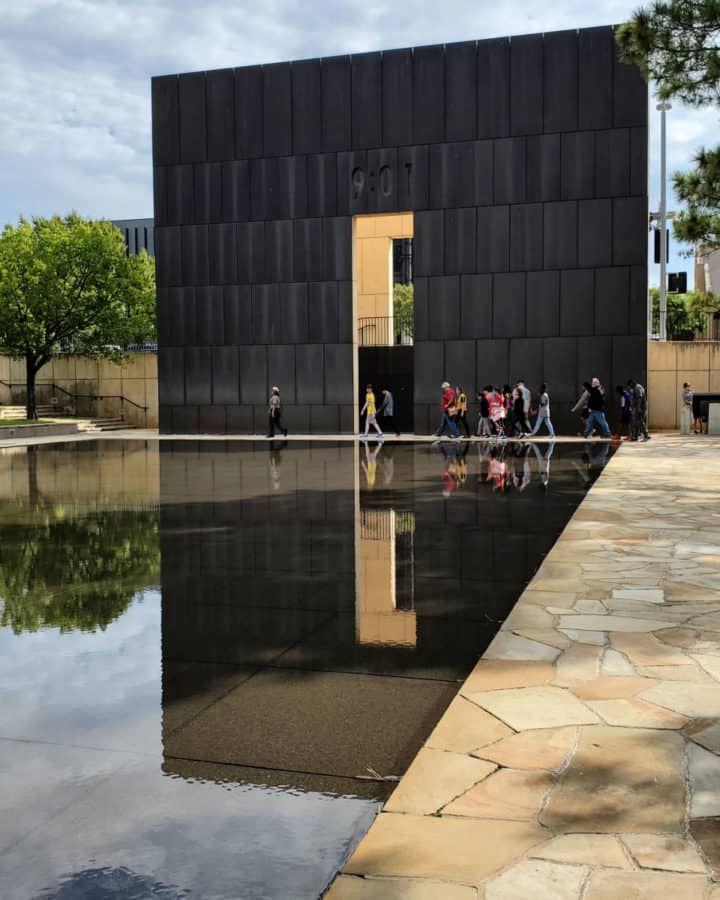 9:01 tower reflecting in the pool with people walking in front of it