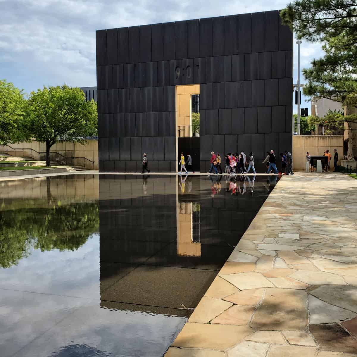 9:01 tower reflecting in the pool with people walking in front of it