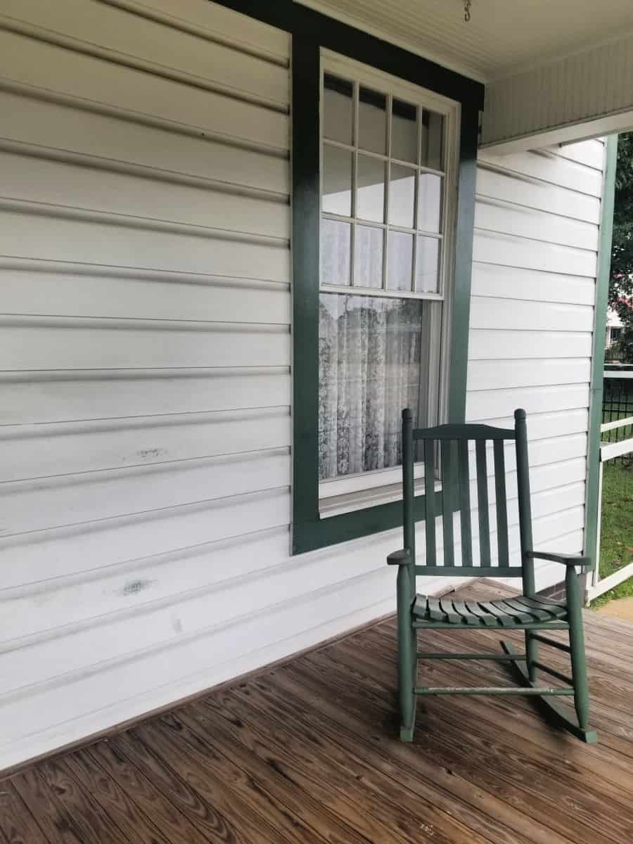 Green rocking chair on the porch next to a window with curtains