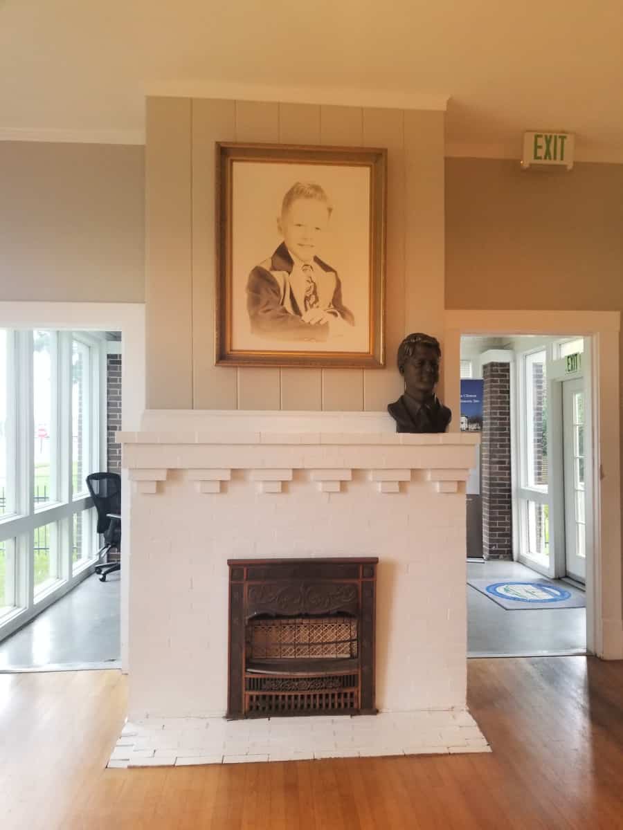framed drawing of bill clinton as a child above a white fireplace with a bust of adult President Clinton on the mantle