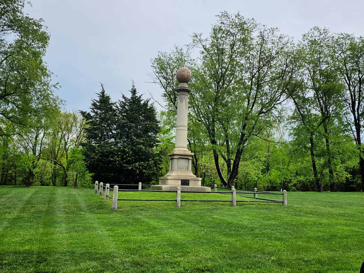 Battlefield memorial statue near a small fence and grassy field