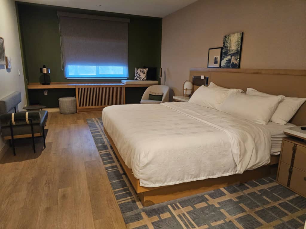 King bed with a headboard, green accent wall with a long counter, chair and lamp in the corner.
