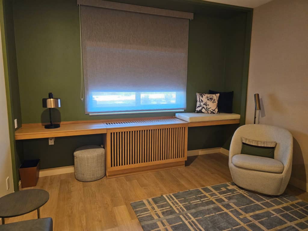 chair and lamp in one corner, long counter with lamp, padded area with pillows, stool under the counter.