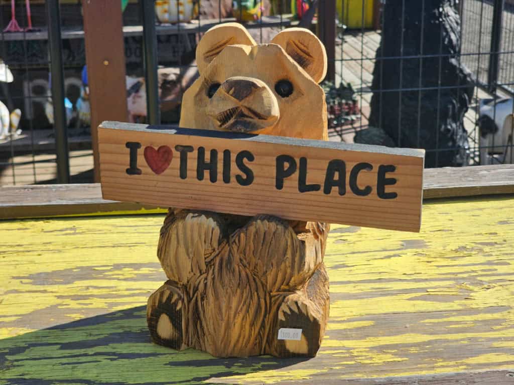 I love this place sign being held by a carved bear