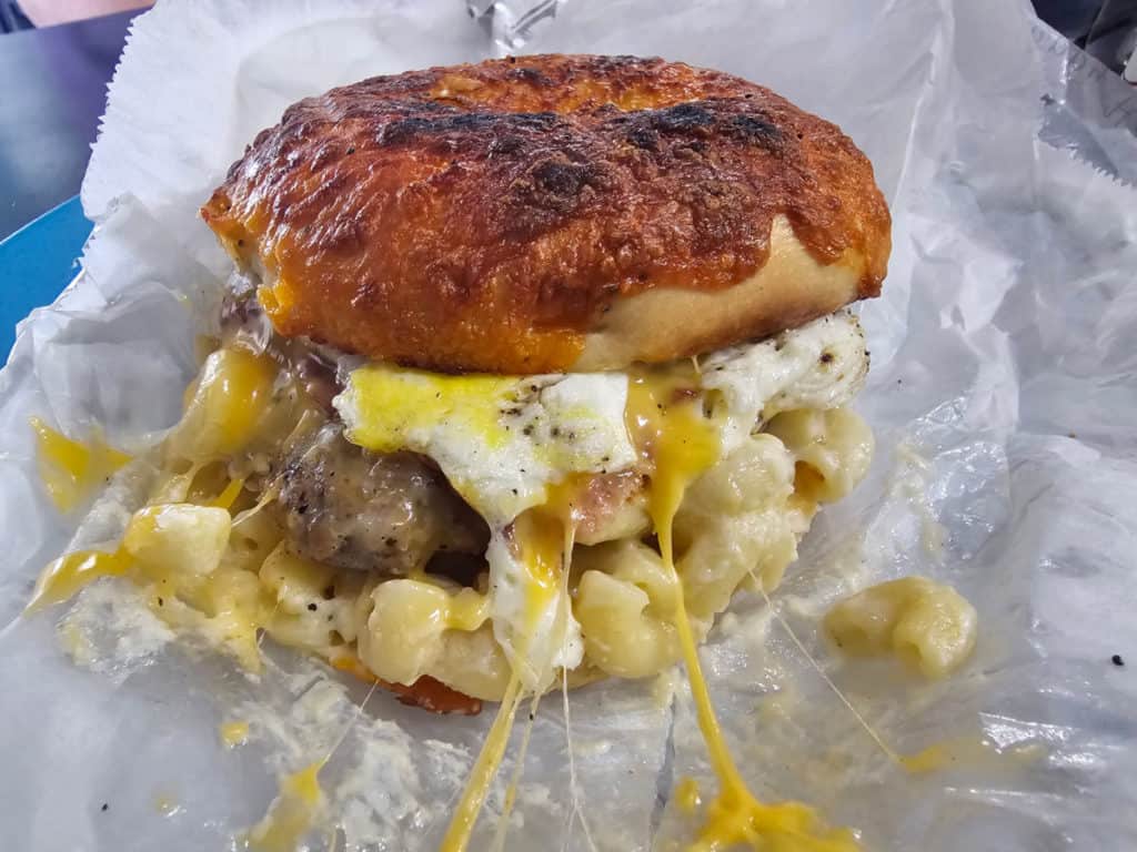 mac and cheese, sausage, and egg on a cheddar bagel