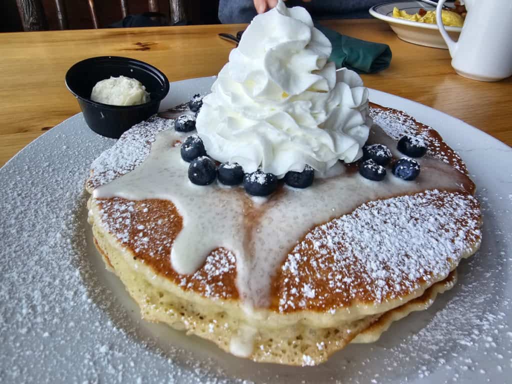 A plate topped with pancakes and blueberries covered in whip cream