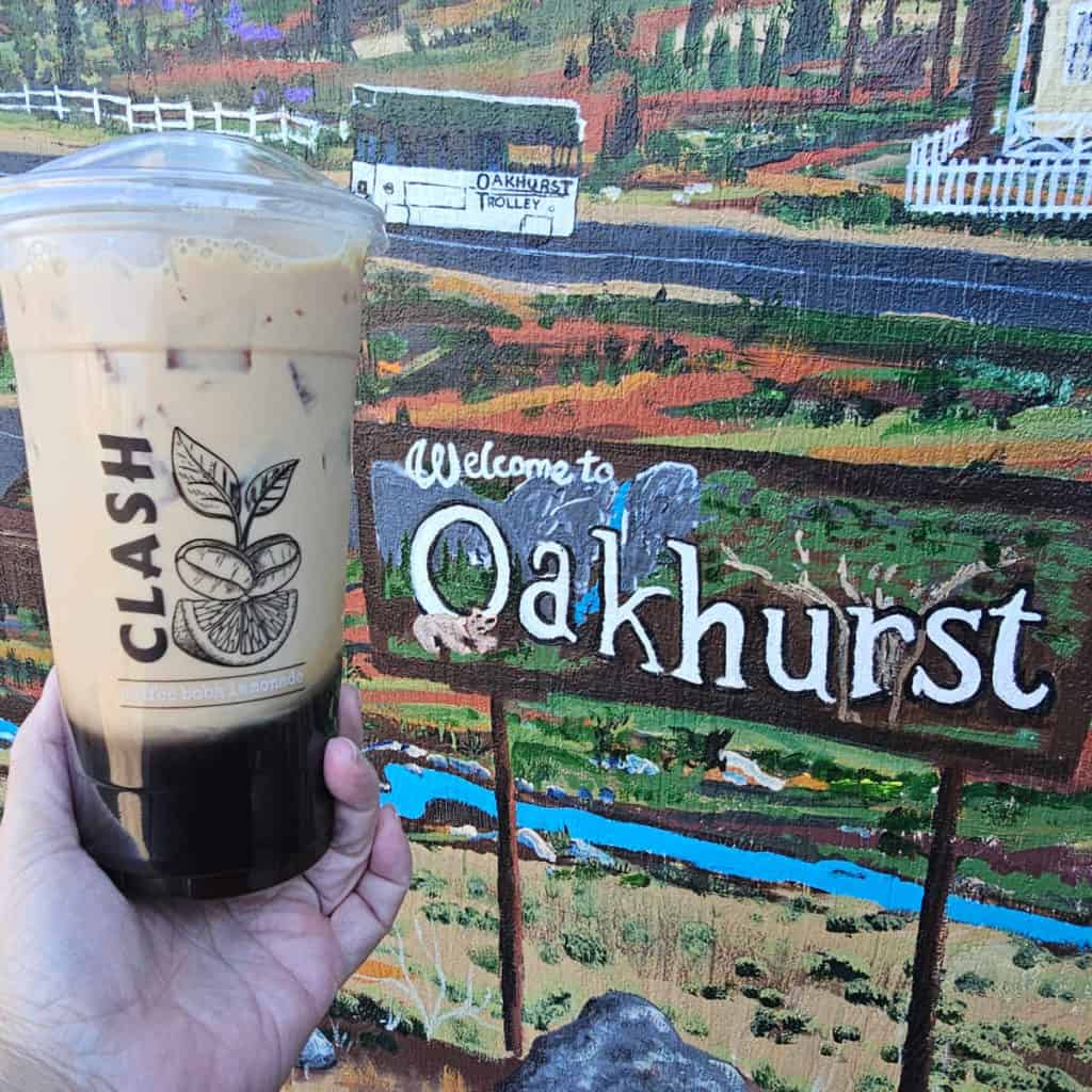 Clash Coffee with chai tea and boba held next to the Welcome to Oakhurst Mural