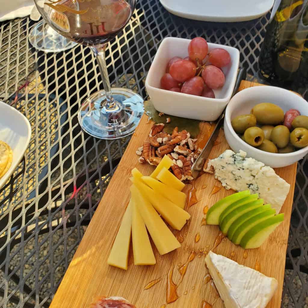 wine glass next to a boat with meat, cheese, olives, and grapes at Idle Hour Winery and Kitchen