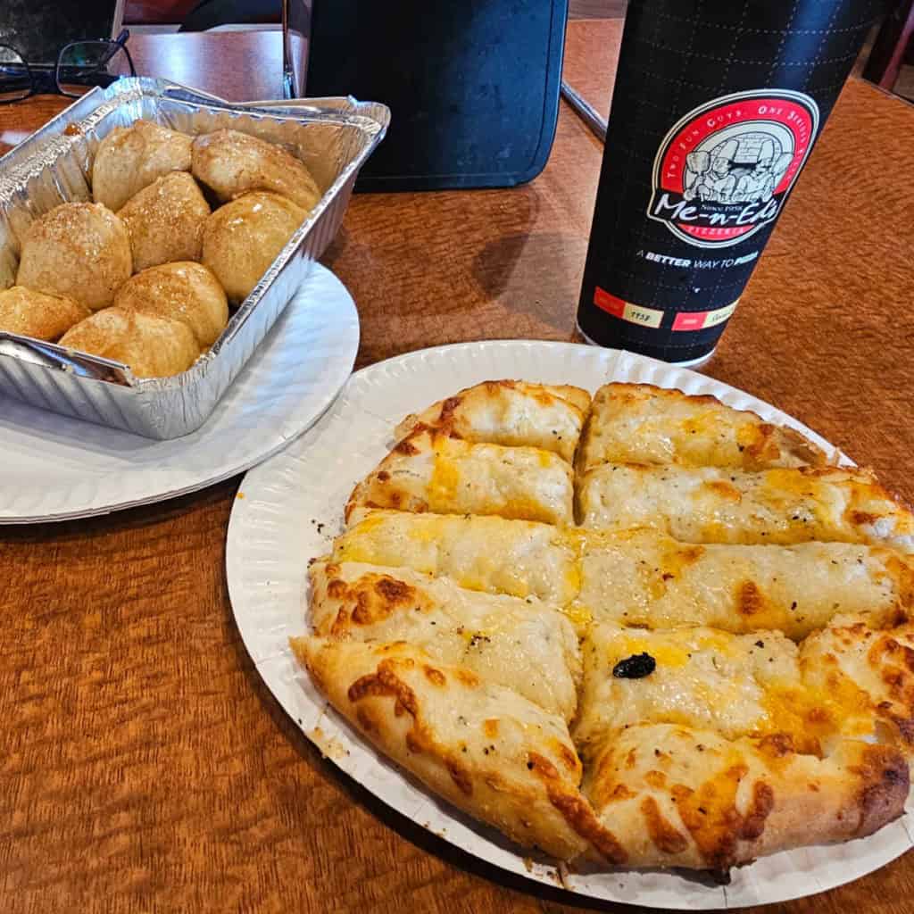 cheese bread on a paper plate next to a Me-n-Ed's cup and a container of cinnamon ball bites